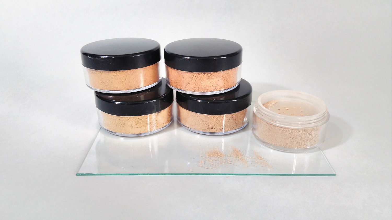 Práškový minerálny makeup v rôznych odtieňoch pleti leží v plastových kelímkoch na bielom pozadí.